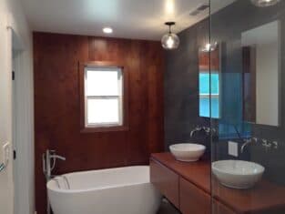 A modern bathroom featuring a freestanding bathtub, wooden accent wall, and double sink vanity, all enhanced by stylish pendant lighting—a perfect example of sophisticated remodeling.