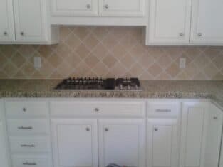 White kitchen cabinets with silver handles, granite countertops, a four-burner gas stove, and beige diamond-patterned tile backsplash create an inviting space. Ideal for commercial construction projects that focus on combining functionality with sleek design.