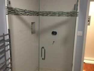 Glass-enclosed corner shower with pebble floor, perfect for showcasing your latest remodeling efforts. White subway tiles and a horizontal accent strip enhance the look, while a built-in niche on the left wall adds functionality.