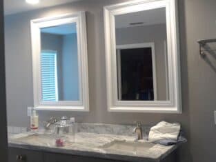 This bathroom features two mirrors above a marble countertop with dual sinks, perfectly folded towels, and a wall-mounted glass jar. It's a testament to exquisite commercial construction, where functionality meets style in every detail.