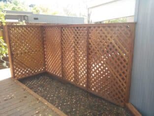 A wooden lattice fence corner graces the deck, casting intricate shadows on the ground. In the background, a commercial construction project unfolds, adding a touch of urban elegance to the scene.