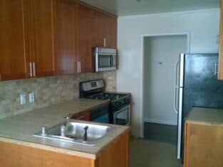 A kitchen with wooden cabinets, stainless steel appliances, a double sink, a tile backsplash, and beige countertops showcases the craftsmanship typical of residential construction.